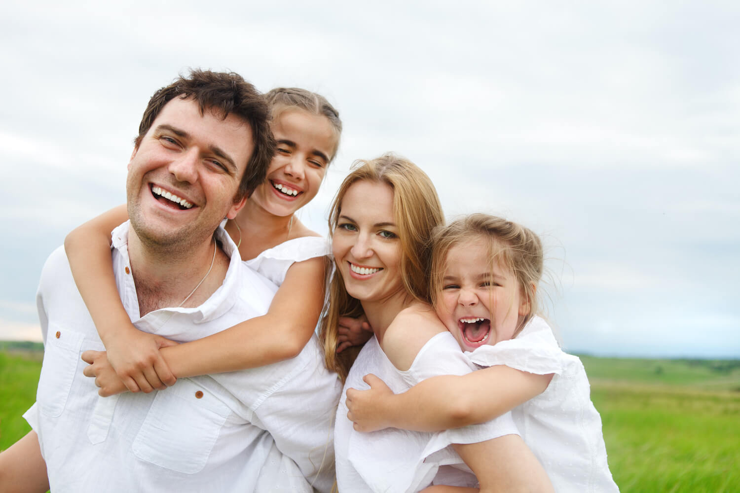 A family of four dressed in white laughing together. 
