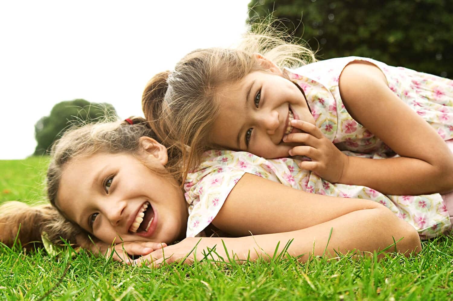 Two young girls laying on the grass and laughing.