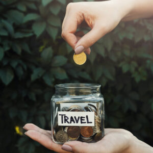 a person dropping coins into a jar marked travel.