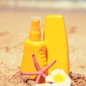 two yellow bottles of sunscreen on a sandy beach with aa tropical flower and star fish.
